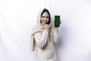 A thoughtful young Asian Muslim woman wearing a hijab and holding her chin while showing the phone screen isolated by a white background photo