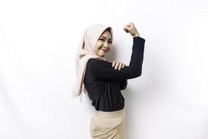 Excited Asian Muslim woman wearing a hijab showing strong gesture by lifting her arms and muscles smiling proudly photo