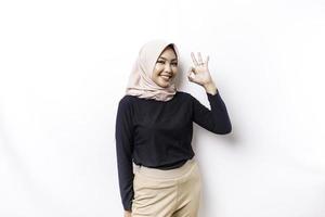 Portrait of a smiling Asian Muslim woman, giving an OK hand gesture isolated over white background photo