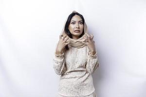 A dissatisfied young Asian Muslim woman looks at the camera posing on a white background, disgruntled girl with irritated face expressions show negative attitude photo