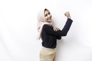 Excited Asian Muslim woman wearing a hijab showing strong gesture by lifting her arms and muscles smiling proudly photo