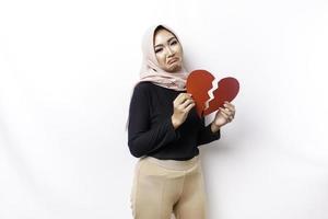 Beautiful young Asian Muslim woman expressed her sadness while holding broken heart isolated on white background photo