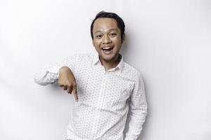 Excited Asian man wearing white shirt pointing at the copy space below him, isolated by white background photo