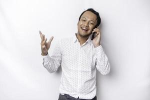 Excited Asian man wearing white shirt smiling while holding his phone, isolated by white background photo
