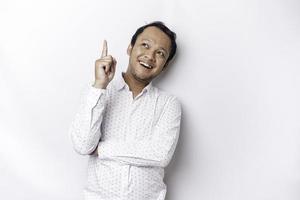 Excited Asian man wearing white shirt pointing at the copy space on top of him, isolated by white background photo