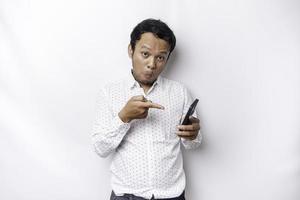 Shocked Asian man wearing a white shirt and holding his phone, isolated by white background photo