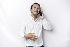 Excited Asian man wearing white shirt smiling while holding his phone, isolated by white background photo