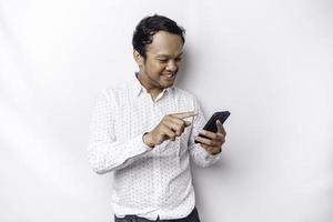 Excited Asian man wearing white shirt smiling while holding his phone, isolated by white background photo