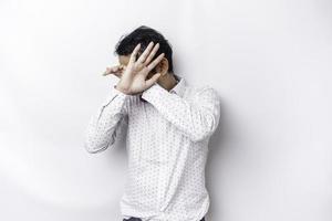 Young scared Asian man isolated on white background, looks depressed, face covered by fingers frightened and nervous. photo