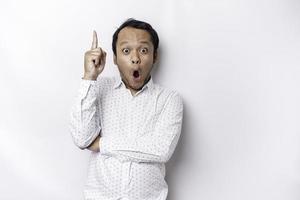 Shocked Asian man wearing white shirt pointing at the copy space on top of him, isolated by white background photo