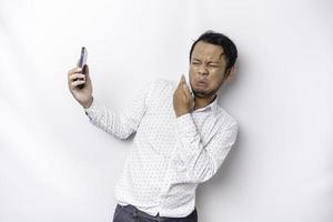 Young Asian man isolated on white background, looks depressed, face covered by arms frightened and nervous while holding his phone photo