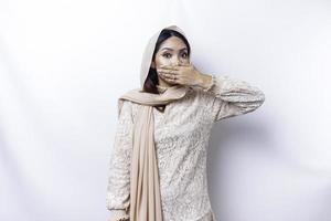 Oops Surprised young Asian Muslim woman covering mouth with hands and staring at camera while standing against white background photo