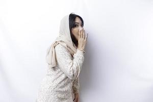 Young beautiful Asian Muslim woman wearing a hijab shouting and screaming loud with a hand on her mouth. communication concept. photo