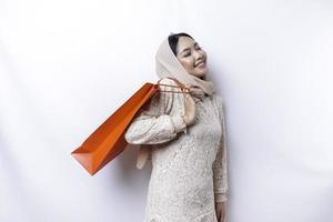 retrato asiático musulmán mujer contento hermosa joven en pie emocionado participación un compras bolsa, estudio Disparo aislado en blanco antecedentes foto