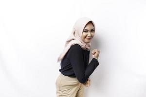 Excited Asian Muslim woman wearing a hijab showing strong gesture by lifting her arms and muscles smiling proudly photo