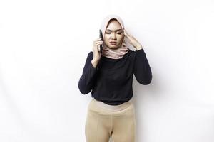 A depresses Asian Muslim woman wearing a hijab looks stressed while talking on the phone isolated by white background photo