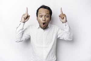 Shocked Asian man wearing white shirt pointing at the copy space on top of him, isolated by white background photo