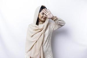 Young Asian Muslim woman isolated on white background, looks depressed, face covered by arms frightened and nervous. photo