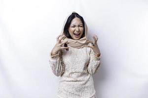 A dissatisfied young Asian Muslim woman looks at the camera posing on a white background, disgruntled girl with irritated face expressions show negative attitude photo