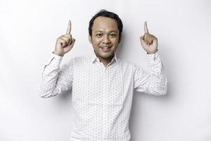 Excited Asian man wearing white shirt pointing at the copy space on top of him, isolated by white background photo