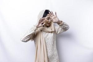 Young Asian Muslim woman isolated on white background, looks depressed, face covered by arms frightened and nervous. photo