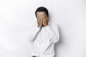 Young scared Asian man isolated on white background, looks depressed, face covered by fingers frightened and nervous. photo