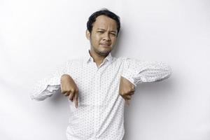 Confused Asian man wearing white shirt pointing down at copy space isolated over white background photo