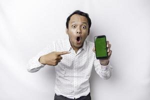 Shocked Asian man wearing a white shirt and showing green screen on his phone, isolated by white background photo