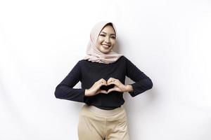 A happy young Asian woman wearing hijab feels romantic shapes heart gesture expresses tender feelings photo