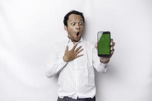 Shocked Asian man wearing a white shirt and showing green screen on his phone, isolated by white background photo