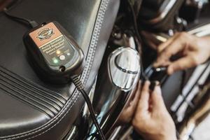 BANGKOK,THAILAND - February 22,2023- Battery Charger Maintainer Trickle for Harley Davidson Motorcycle on seat with hand connect the tender plug to motorcycle background at garage. photo