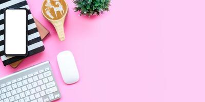 Office desk with computer keyboard, Blank screen smart phone, mouse, Notebook, Cup of coffee on pink background, Top view with copy space, Mock up. photo