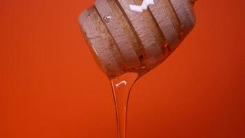 Honey slowly drips from a honey spoon on an orange background video