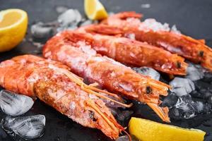Frozen seafood. Fresh shrimps with lemon on dark background. Red raw prawns photo