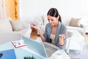 Smiling young woman using laptop at home, looking at screen, chatting, wearing wireless headset having video conference . business trainer tutoring by webcam, online training, e-coaching concept photo