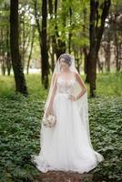 retrato de un elegante novia niña en un camino en un caduco bosque con un ramo de flores foto