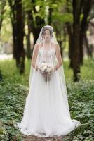 retrato de un elegante novia niña en un camino en un caduco bosque con un ramo de flores foto