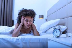 Sleepless and desperate beautiful caucasian woman awake at night not able to sleep, feeling frustrated and worried looking at clock suffering from insomnia in sleep disorder concept. photo