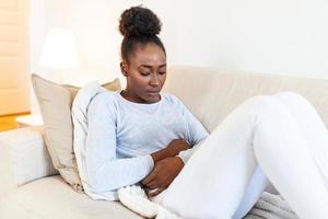 Woman lying on sofa looking sick in the living room. Beautiful young woman lying on bed and holding hands on her stomach. Woman having painful stomachache on bed, Menstrual period photo