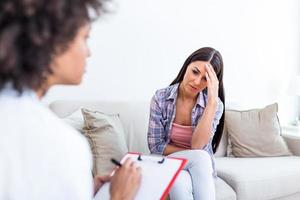 mujer joven sentada en el sofá cubriéndose la cara con las manos, sintiéndose desesperanzada, deprimida o llorando, visitando a un psicoterapeuta, descubriendo un mal diagnóstico o resultados de pruebas médicas foto