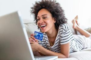 hembra consumidor gasto comprando en Internet, estilo de vida. contento mujer compras en línea con ordenador portátil a hogar. mujer utilizando ordenador portátil computadora compras en línea, utilizando crédito tarjeta jugando en línea, sonriente adentro foto