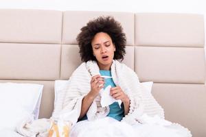 Sickness, seasonal virus problem concept. Woman being sick having flu lying on bed looking at temperature on thermometer. Sick woman lying in bed with high fever. Cold flu coronavirus, covid19 photo