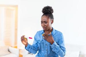 Shocked woman looking at control line on pregnancy test. Single sad woman complaining holding a pregnancy test . Depressed Black girl holding negative pregnancy test. photo