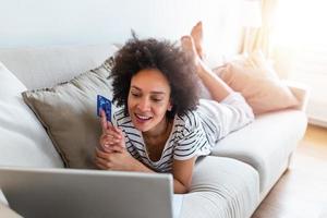 Internet payment. Happy cheerful woman looking at the Internet screen while making an Internet payment. Happy young woman with credit card and laptop sitting on sofa at home. Online payment photo