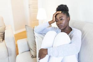 Sad thoughtful worried african american girl sit on sofa looking away feel depressed doubtful, lonely stressed upset young black girl thinking of psychological problem thinking regret about mistake photo