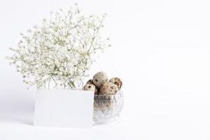 Easter white monochrome card. Gypsophila vase, empty white blank note, quail eggs in crystal bowl. photo