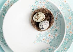 Two quail eggs in nest on light blue plates with floral pattern. Easter mock up on plate. Close up. photo