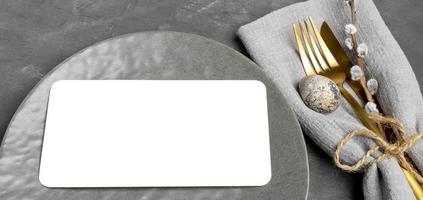 Plate with white blank sheet, golden cutlery, quail egg, willow twig on gray Banner Mock up Close up photo