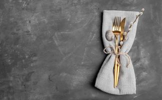 Linen napkin with golden cutlery, quail egg, willow twig on gray. Easter. Top view. Copy space. photo