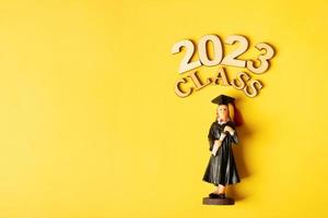 Class of 2023 concept. Wooden number 2023 with graduate statuette on color background photo